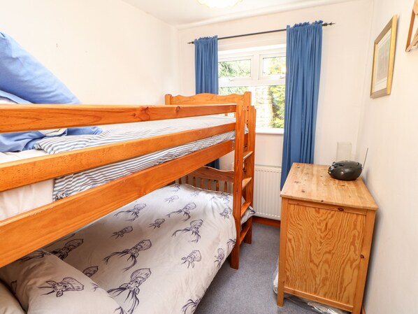 A bunk bed with striped bedding, a small wooden desk, a framed picture on the wall, and a window with blue curtains. - Hunter Cottage (Haltwhistle)