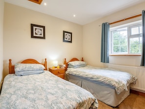 Two single beds with matching floral-patterned bedding, each with a nightstand, lamp, and small table with a book and refreshments.