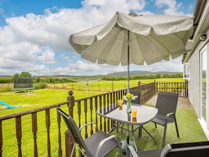 Enjoy a serene view of the lush green field and distant hills from this balcony, complete with a table for two and a shaded seating area.