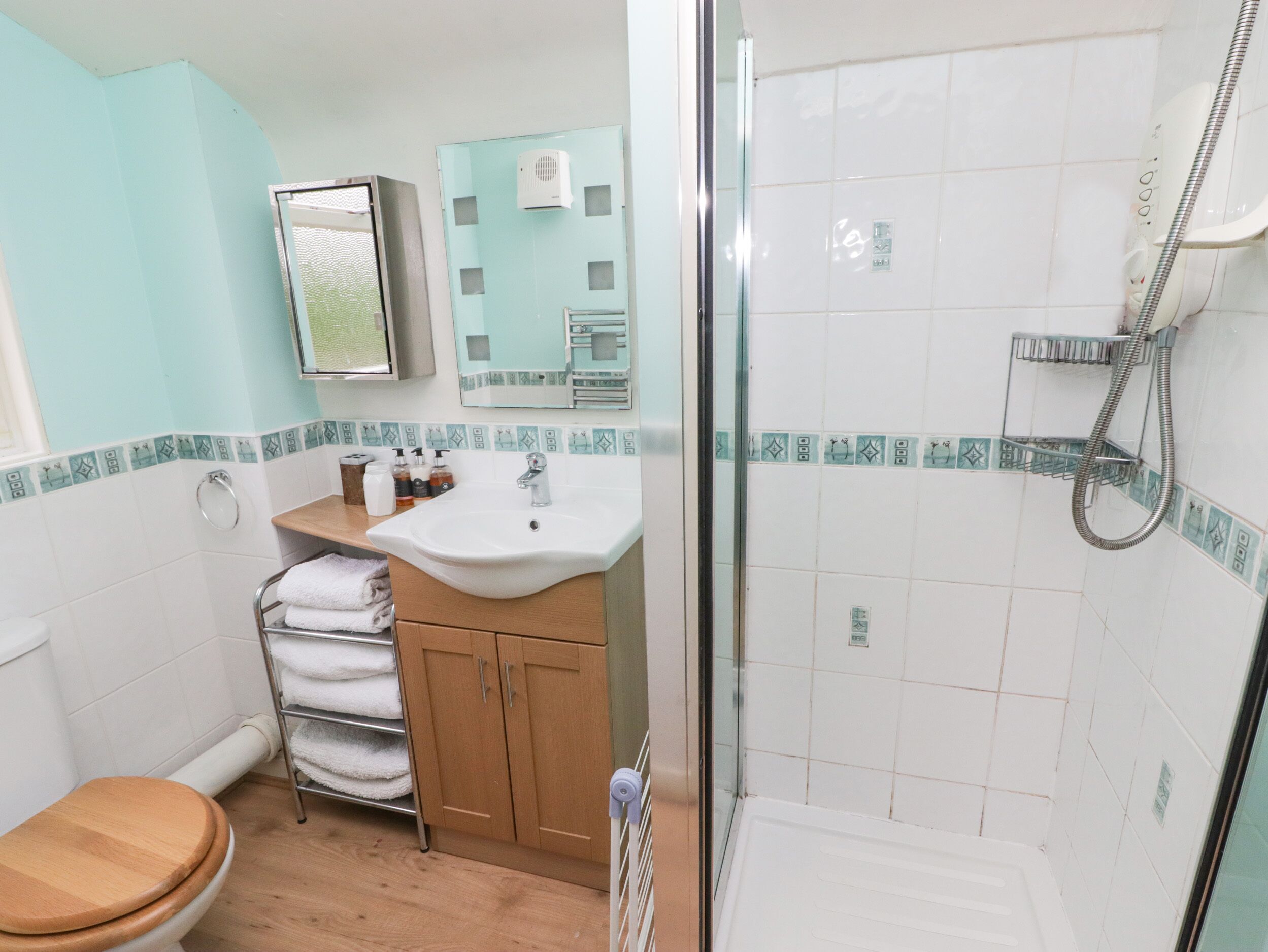 Une salle de bain avec des toilettes en bois, un lavabo avec un miroir au-dessus, une douche avec un flexible et un porte-serviettes avec des serviettes pliées.