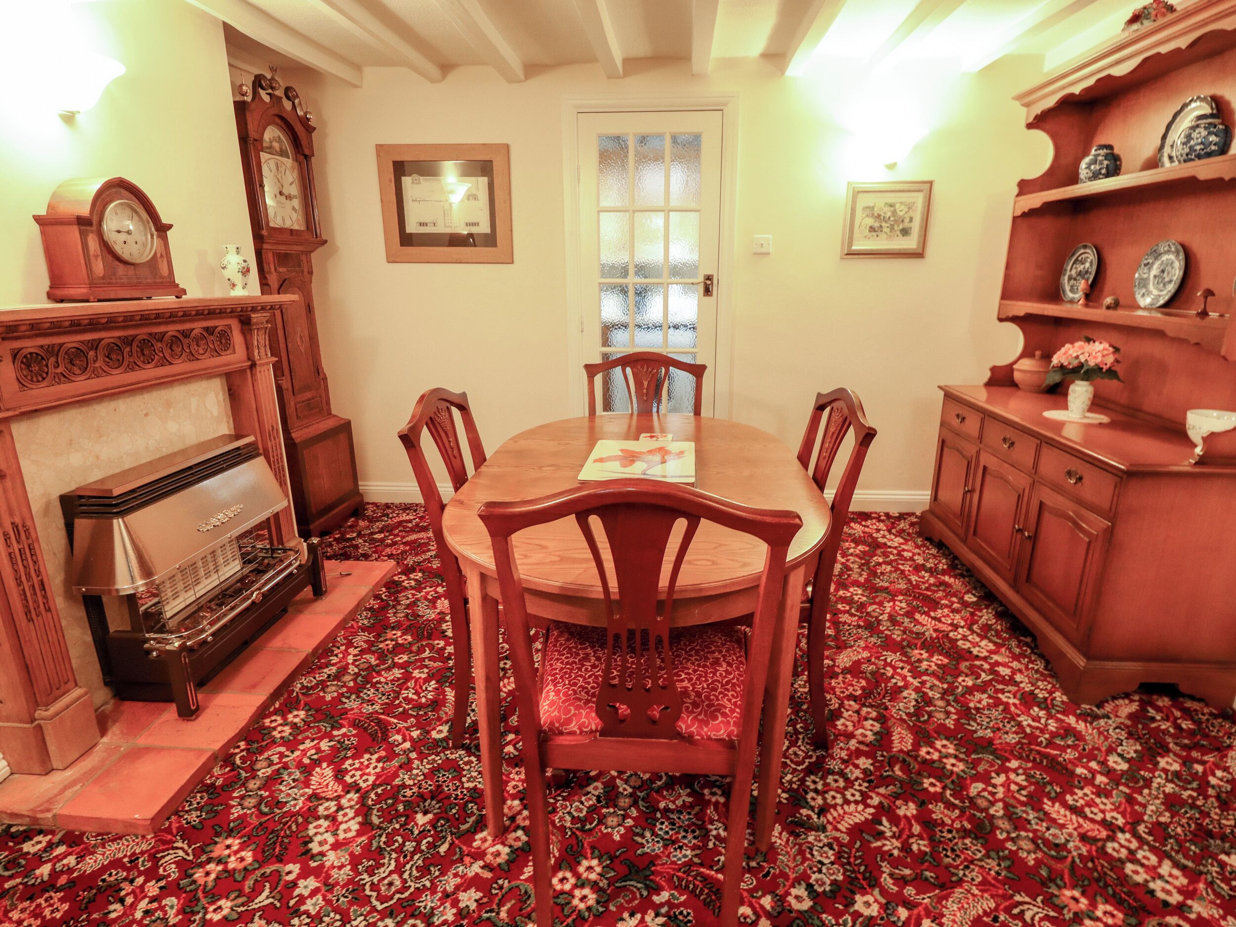 A dining room with a wooden table and chairs, a fireplace, a clock, and a door with frosted glass panels.