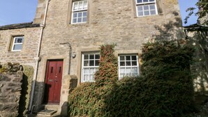 Un bâtiment en pierre avec une porte rouge, deux fenêtres et un petit porche.