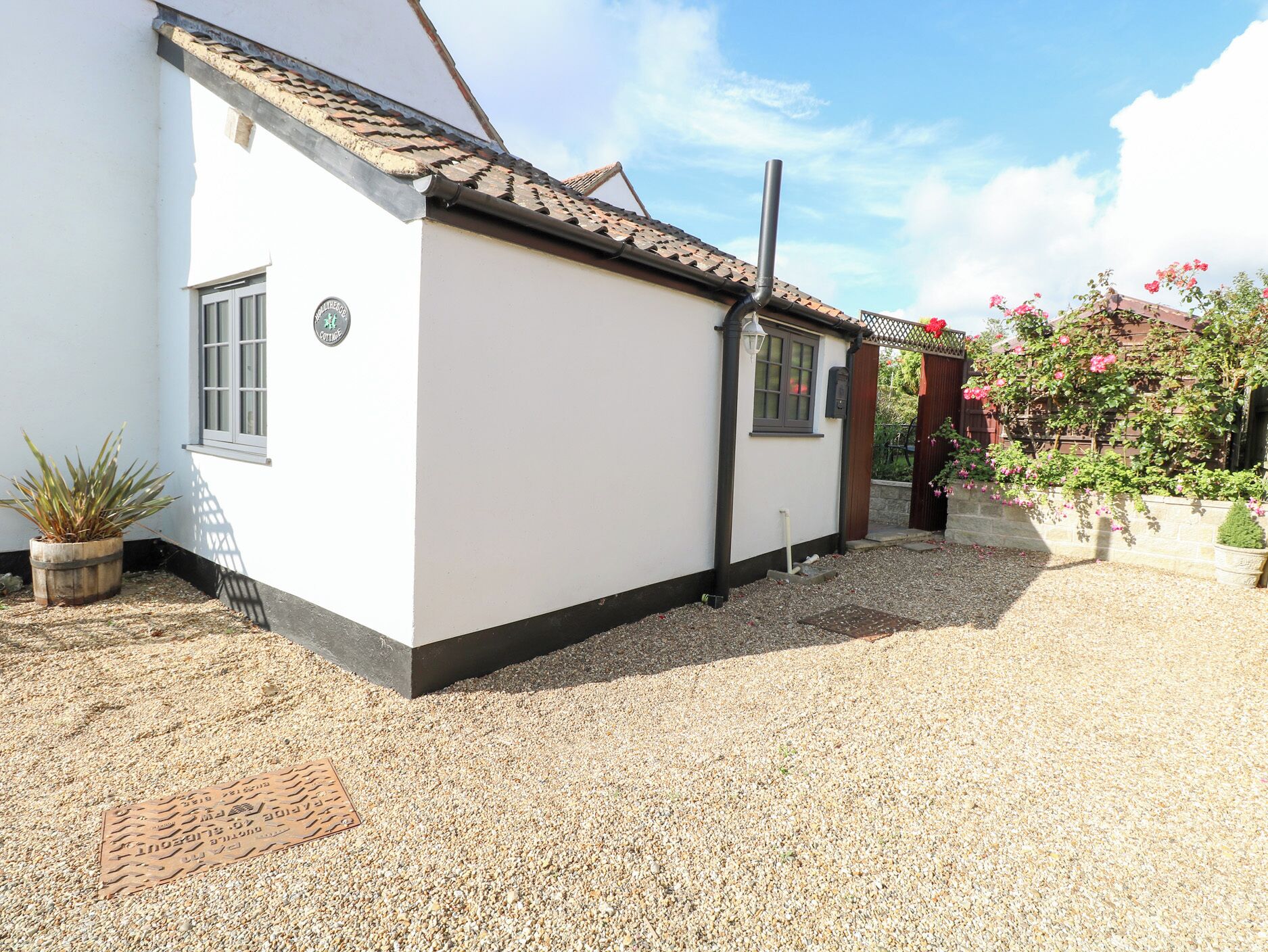 A white building with a tiled roof, a gravel driveway, and a potted plant.