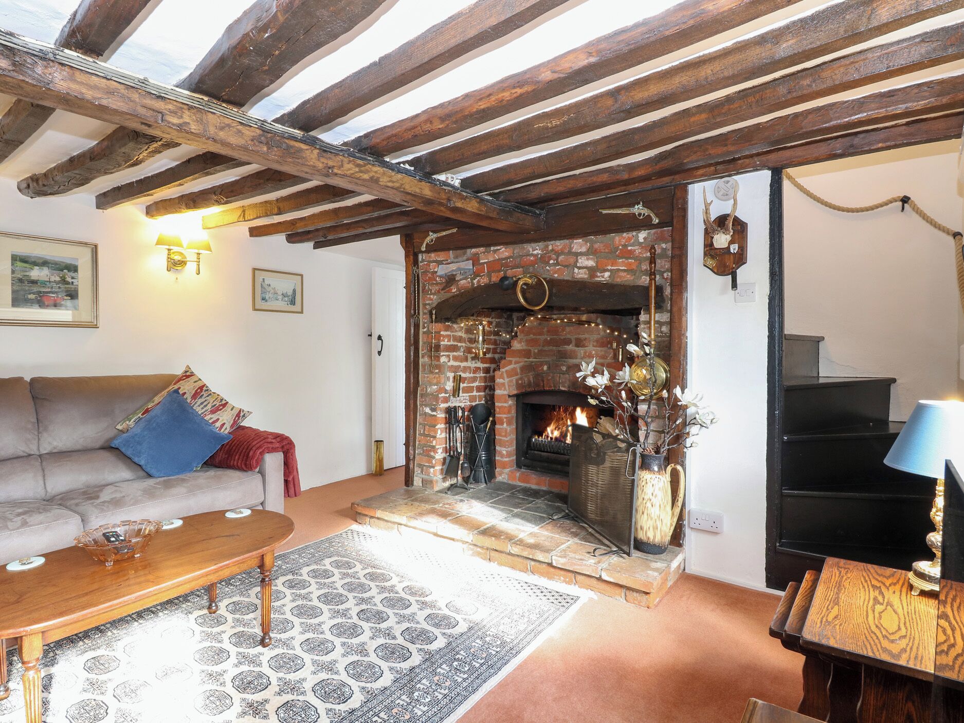 Ein gemütliches Wohnzimmer mit freiliegenden Holzbalken, einem Kamin aus Backsteinen, einem Sofa und einem Couchtisch.