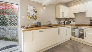 A modern kitchen with white cabinets, a wooden countertop, a built-in oven, and a microwave. - 2 Bryn Tirion (Blaenau Ffestiniog)