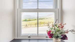 A window with a view of a rural landscape, a vase with flowers on a windowsill, and a white wall. - 2 Bryn Tirion (Blaenau Ffestiniog)