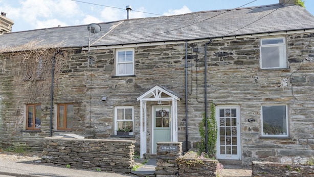 A stone house with a gabled roof, a front door with a heart-shaped knocker, and a sign reading "2 Brgn Trion." - 2 Bryn Tirion (Blaenau Ffestiniog)