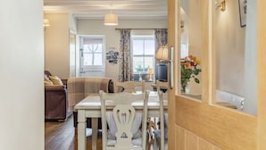 A dining area with a white table and chairs, a brown sofa, and a television in the background. - 2 Bryn Tirion (Blaenau Ffestiniog)