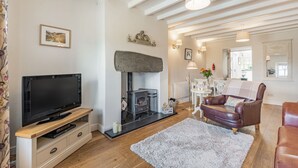 A living room with a TV on a wooden stand, a fireplace, a brown leather sofa, and a white rug. - 2 Bryn Tirion (Blaenau Ffestiniog)