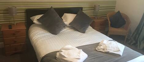 A neatly made bed with pillows, a folded towel, and a bedside lamp on a wooden nightstand.