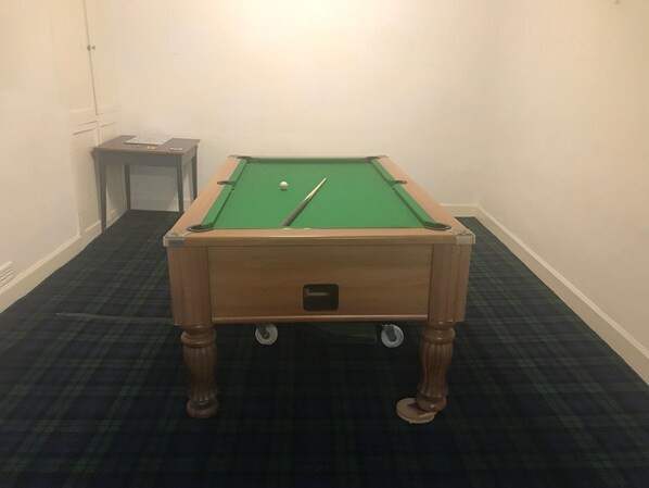 A pool table with a green felt surface, a cue stick, and a white cue ball. - Crown Hotel (Langholm)