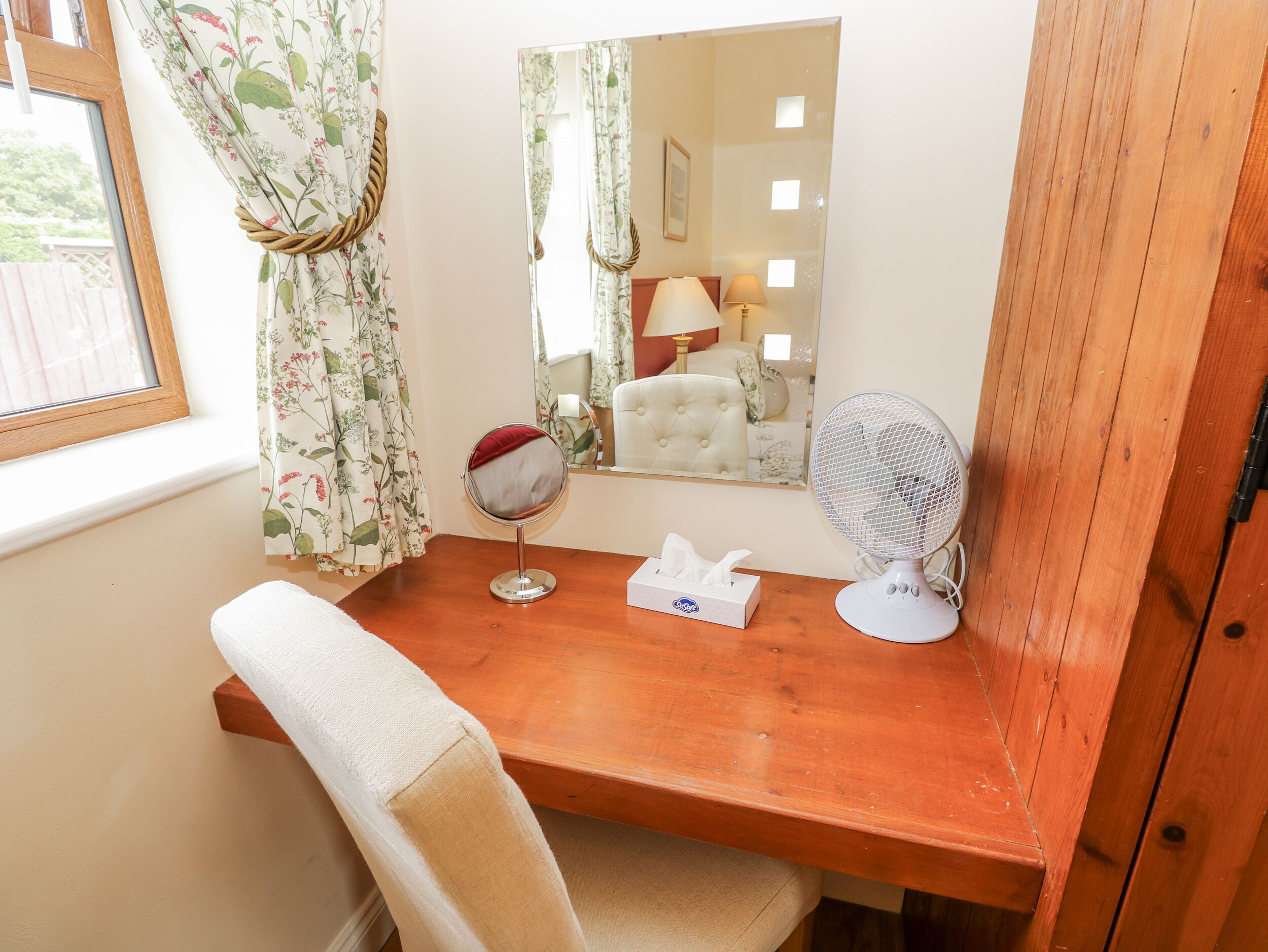 A wooden desk with a mirror, a fan, and a tissue box.
