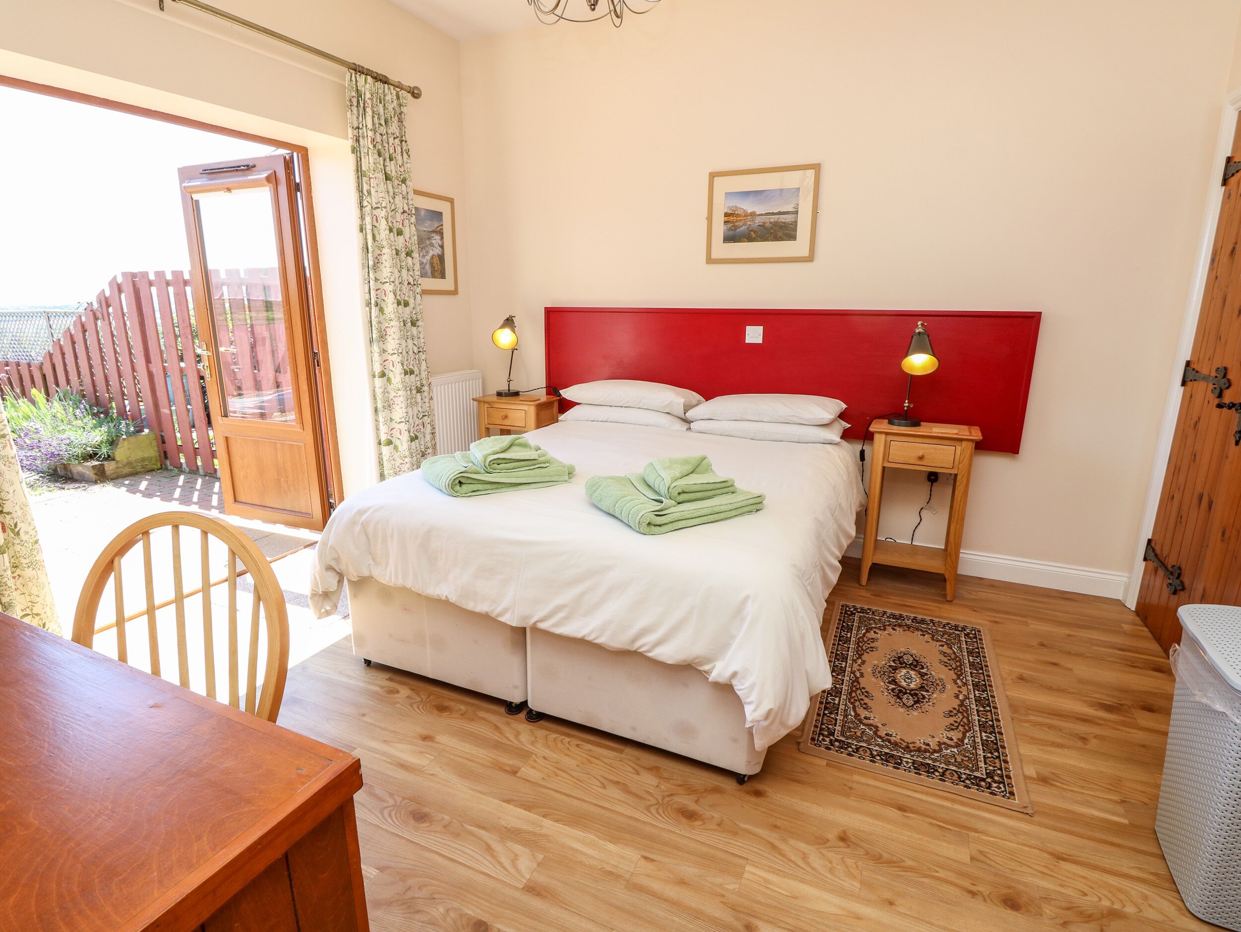 A bedroom with a bed, two bedside tables, a nightstand, a wooden chair, a table, and a view of the outside.