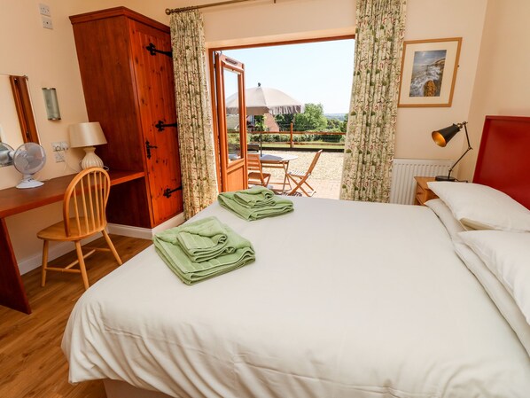 Una habitación de hotel con cama, escritorio con silla, ventilador y vistas al exterior.