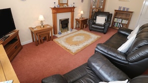 A living room with a fireplace, leather sofa, wooden coffee table, and a television. - Penelope (Tyn-y-Gongl)
