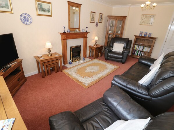 A living room with a fireplace, leather sofa, wooden coffee table, and a television. - Penelope (Tyn-y-Gongl)