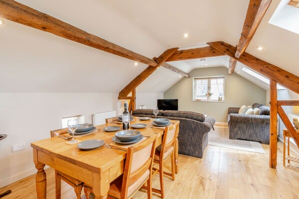 A dining area with a wooden table set for four, a sofa, and a television in the background. - Upstairs Downstairs Cottage (Scarborough)