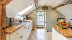 A kitchen with wooden beams, a skylight, a fruit bowl, and a view through a door. - Upstairs Downstairs Cottage (Scarborough)