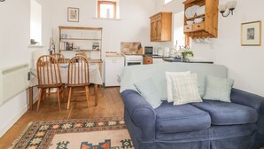 Ein gemütliches Wohnzimmer mit einem blauen Sofa, Holzstühlen, einem gemusterten Teppich und einer Küchenzeile mit Holdekor und einem Fenster.