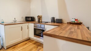 A compact kitchen with white cabinets, a wooden countertop, a microwave, a toaster, and a coffee maker. - Lair Close Cottage (Harrogate)