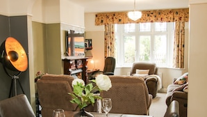 A dining area with a table set for two, a vase with flowers, and a bookshelf in the background.
