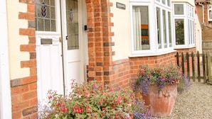 A house with a white door, a brick archway, and a large flower pot with red and purple flowers.