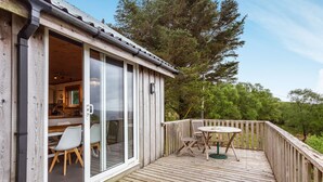 A wooden deck with a table and chairs, a sliding glass door leading to a room with a kitchen area visible. - Thorsvik (Sleat)