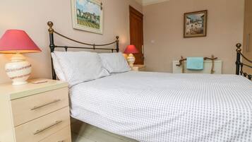 Un dormitorio ordenado con cama, mesitas de noche, lámpara, cómoda y dos cuadros en las paredes.