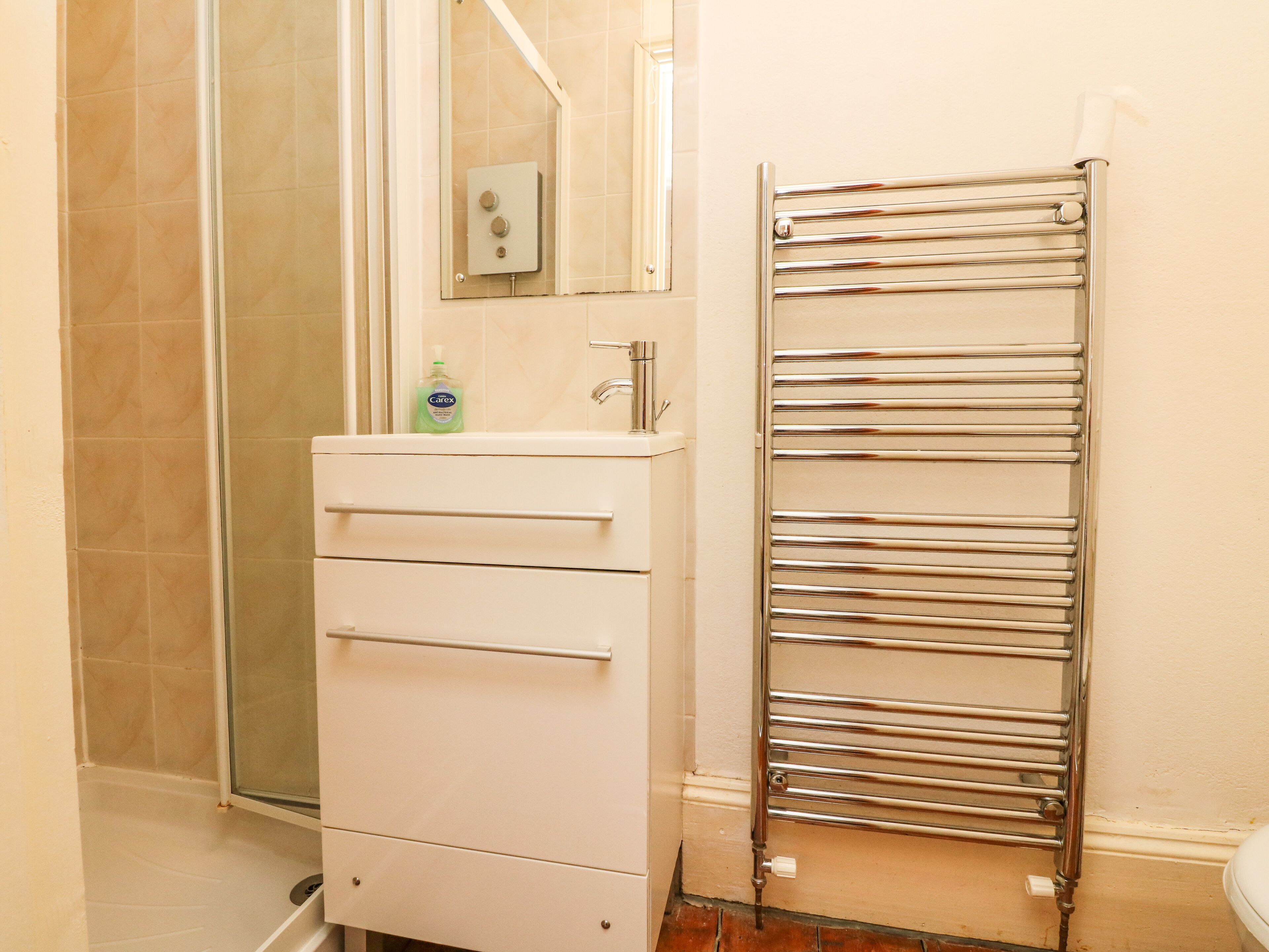 Un baño con cabina de ducha de vidrio, un mueble blanco con cajones, un toallero cromado y un inodoro.