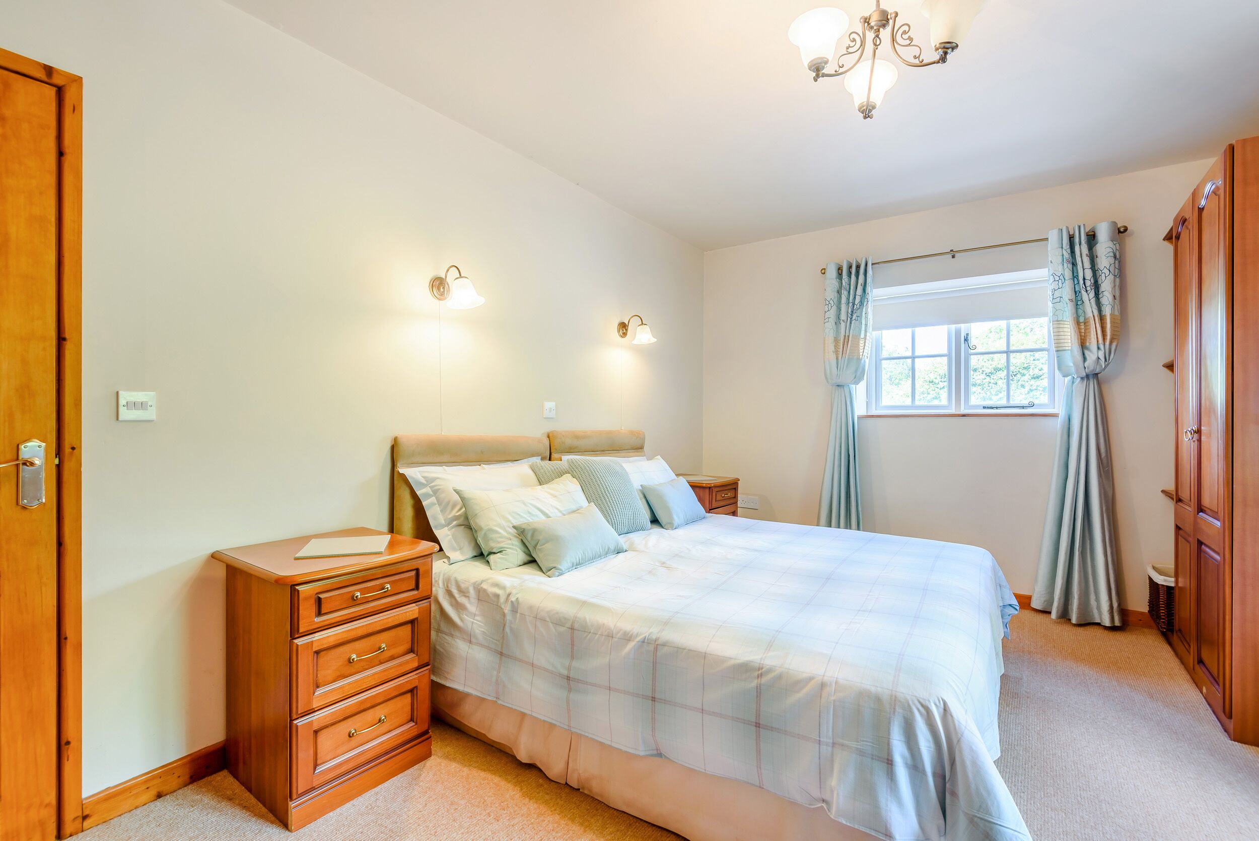 A bedroom with a large bed, wooden nightstands, a dresser, and a window with curtains.