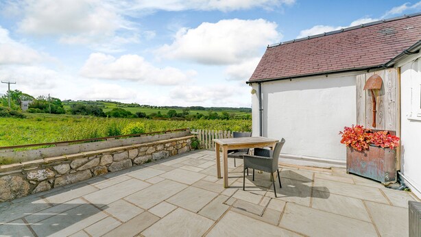 Une terrasse avec une table et des chaises, un mur en pierre et une vue sur un champ verdoyant.