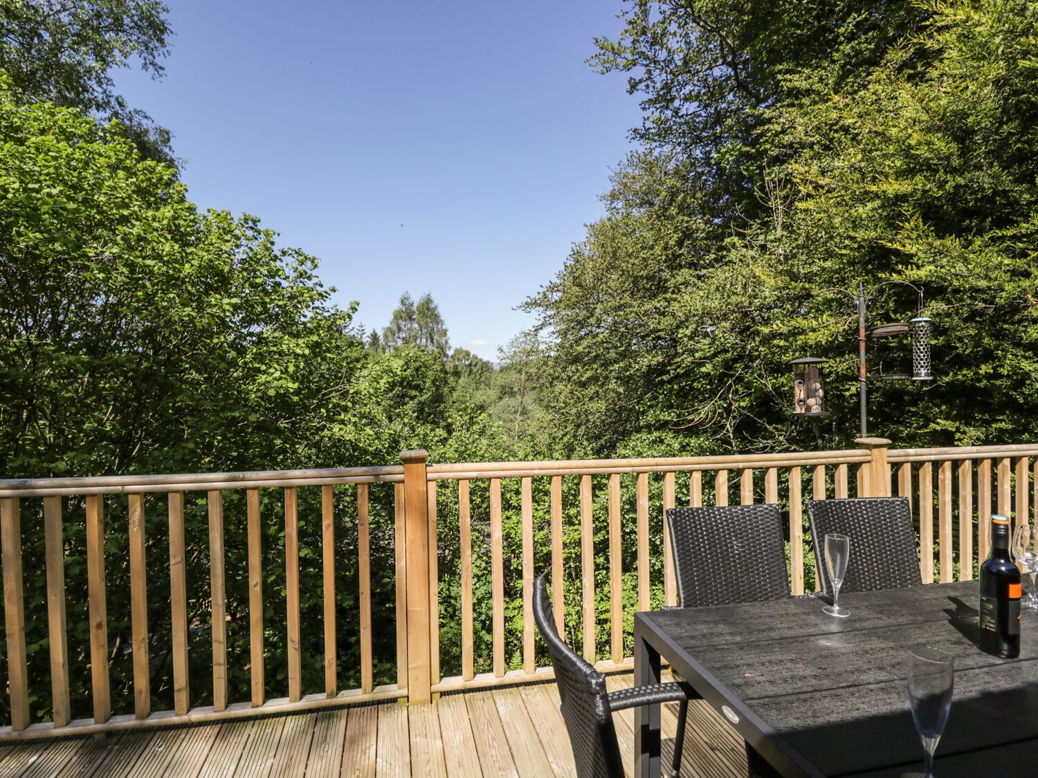 A wooden deck with a table and chairs, surrounded by dense green foliage.