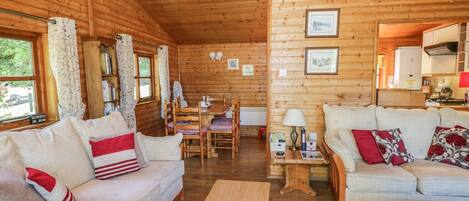 A cozy log cabin interior with a sofa, a wooden coffee table, and a dining area with a table and chairs.