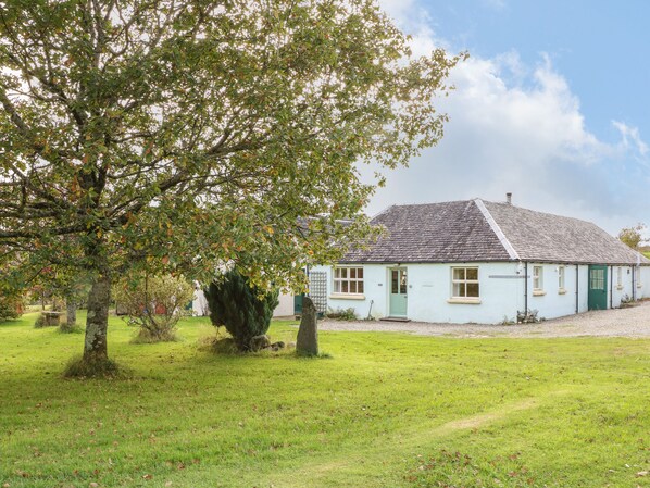 Ein hellblaues Haus mit geneigtem Dach, umgeben von einem Rasen und einem großen Baum.