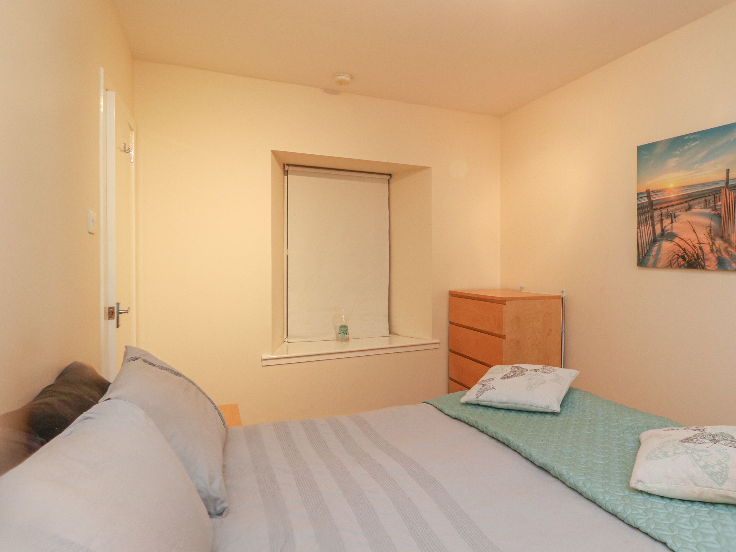 A bedroom with a bed, a dresser, a window, and a painting on the wall.