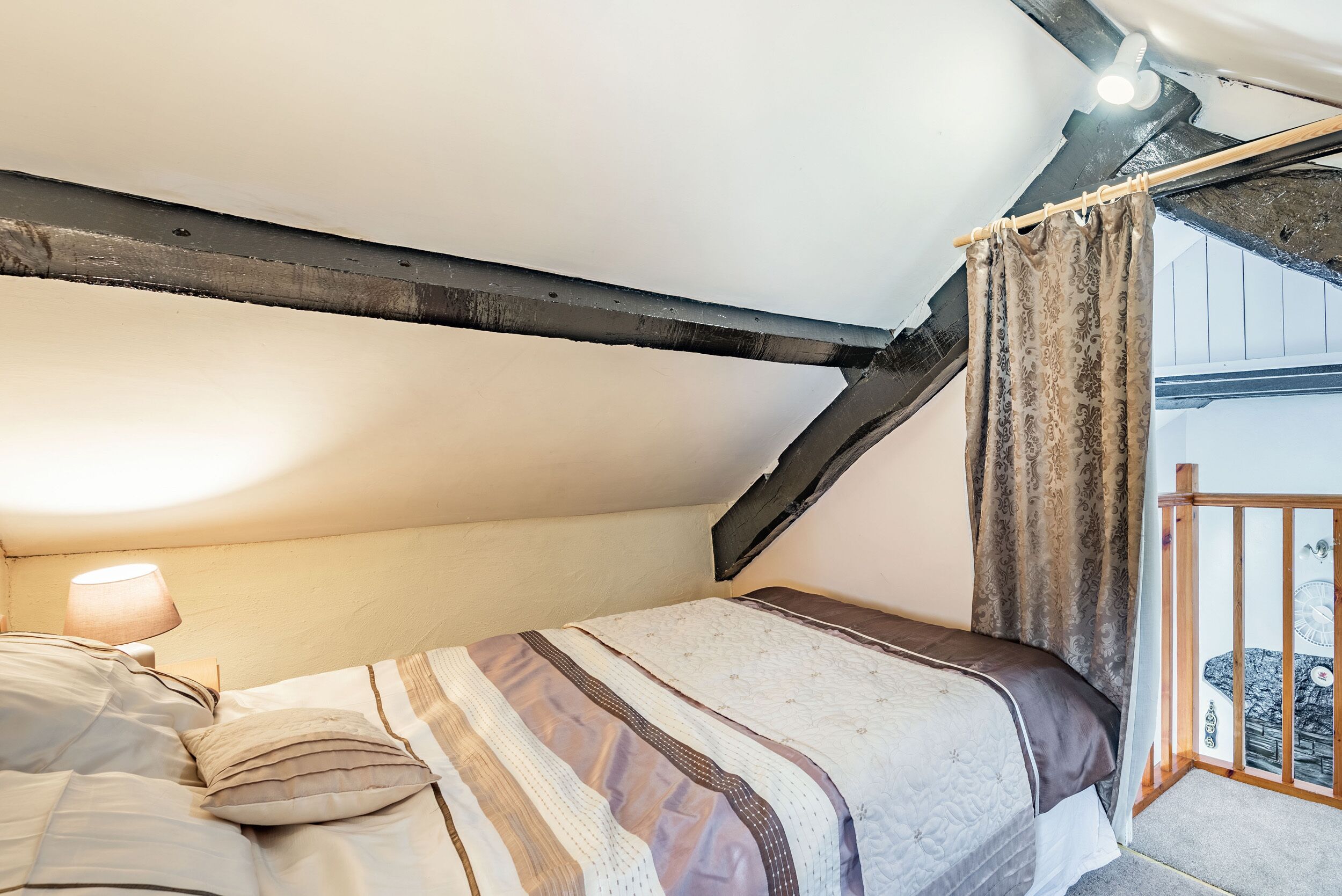 Un dormitorio con cama, mesita de noche, lámpara y ventana con cortinas.