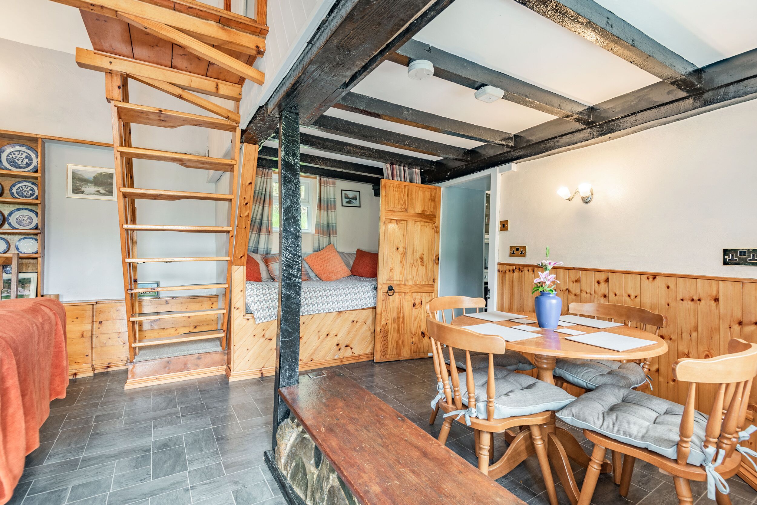 A cozy room with a loft bed, wooden ladder, and a dining area with a table and chairs.