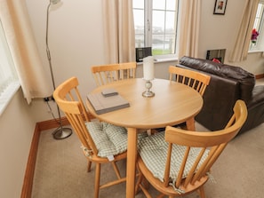 A cozy living room with a round wooden table, four wooden chairs, a brown leather sofa, and a window with curtains. - White Rock Cottage (Chathill)