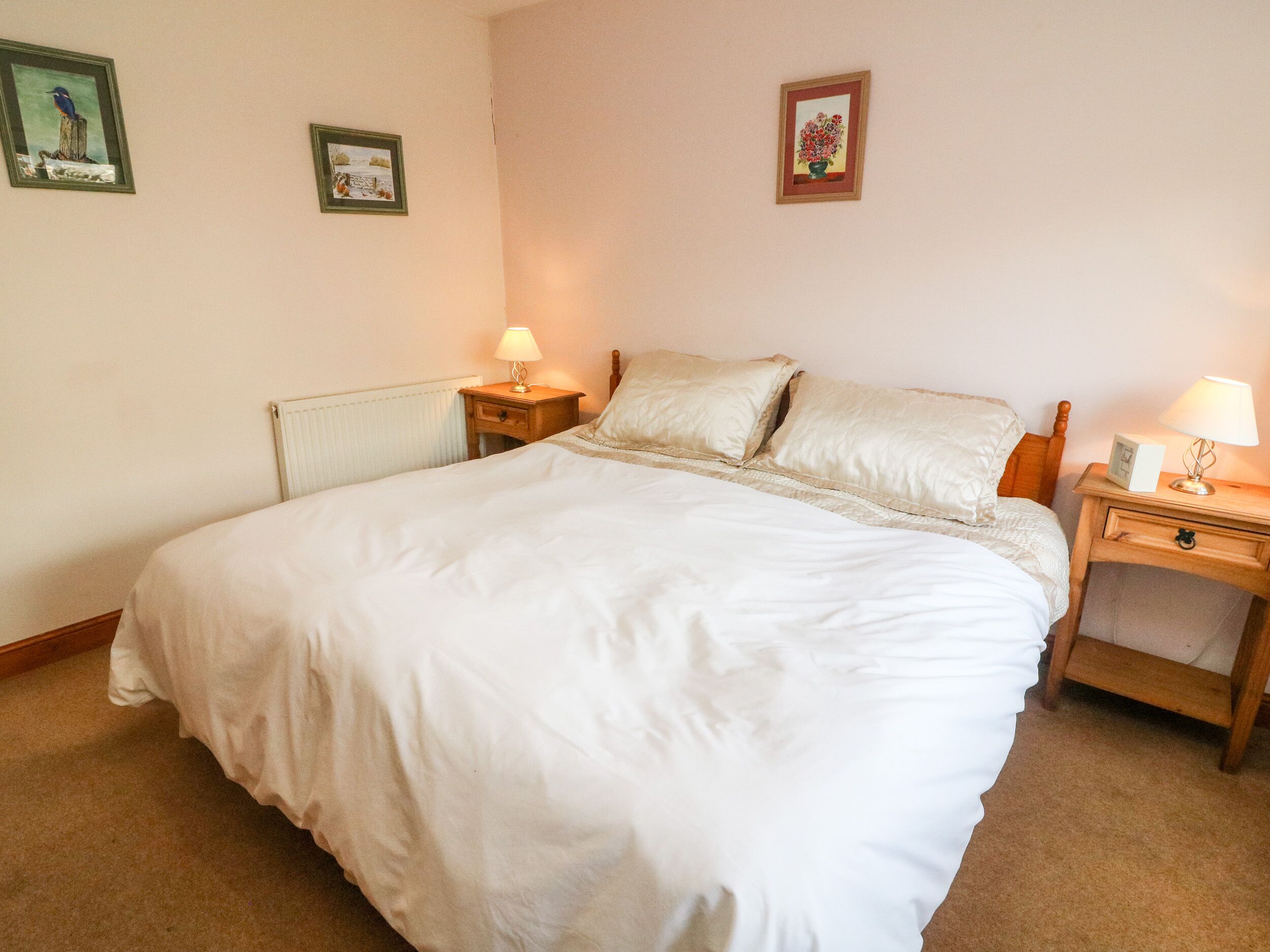 Una cama bien hecha con ropa de cama blanca, dos mesitas de noche con lámparas y dos cuadros en la pared.