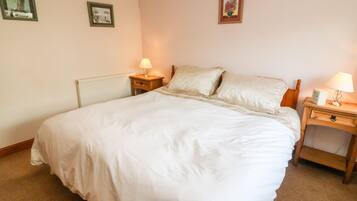 Una cama bien hecha con ropa de cama blanca, dos mesitas de noche con lámparas y dos cuadros en la pared.