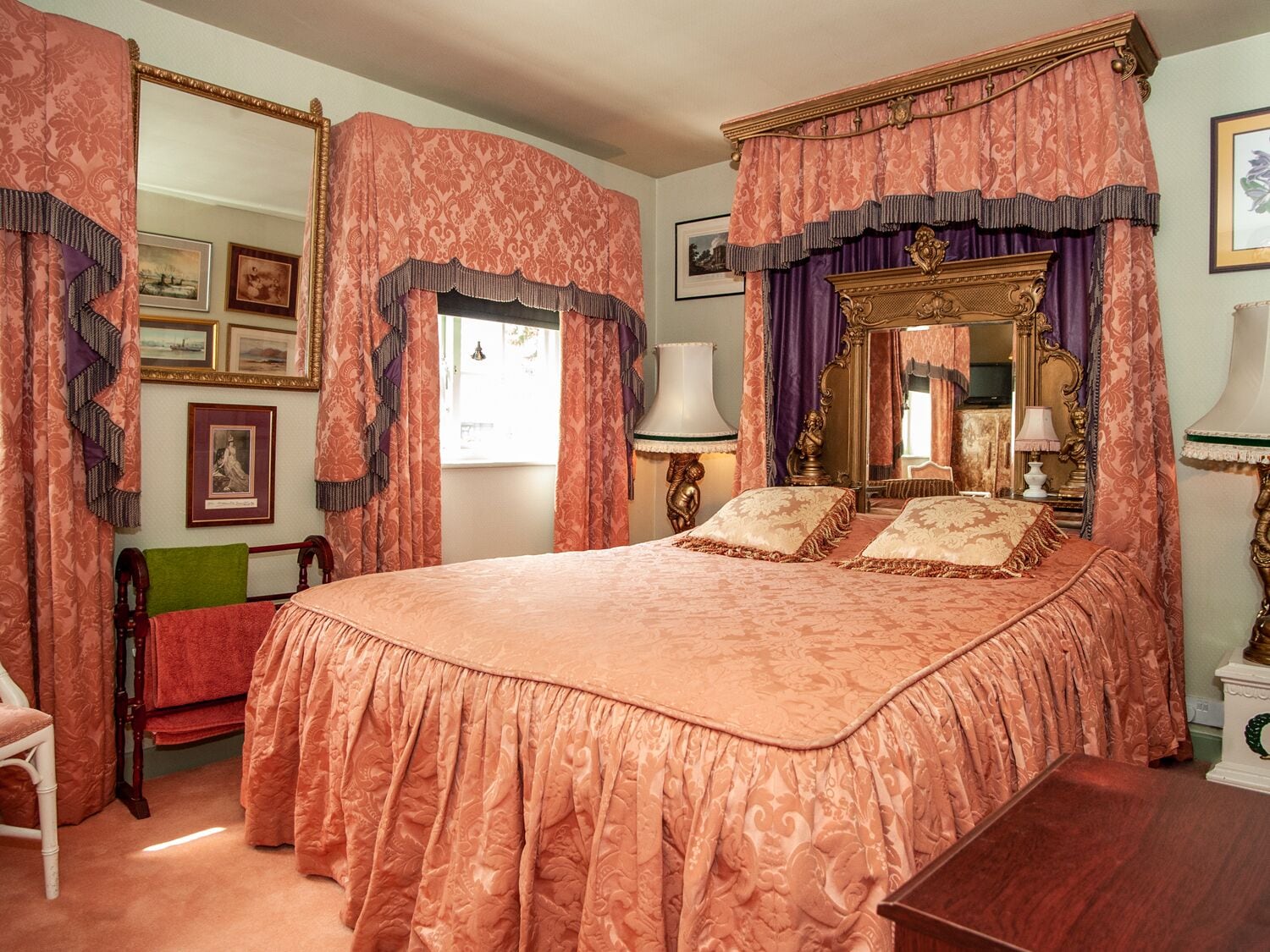 A bedroom with a large bed, ornate curtains, and a mirror with a gold frame.