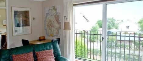 A living room with a green leather sofa, a dining table, and a large sliding glass door leading to a balcony.