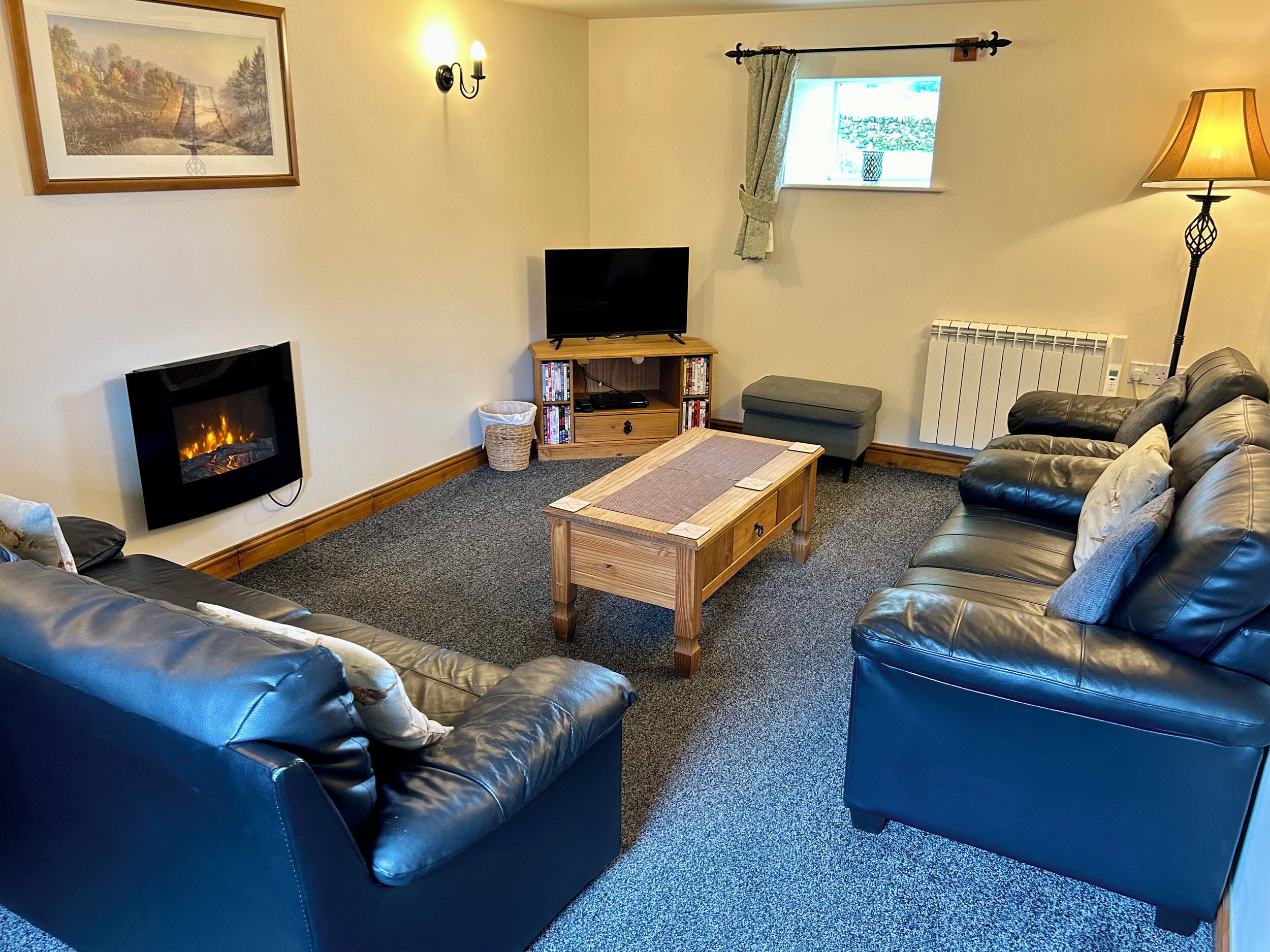 A living room with a fireplace, leather sofas, a coffee table, a TV, and a bookshelf.