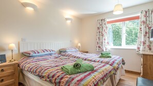 A double room with two beds, bedside lamps, a desk, and a window with curtains.
