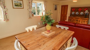 A dining area with a wooden table, white chairs, a vase with flowers, and a red sofa. - Hill Top Cottage (Lincoln)