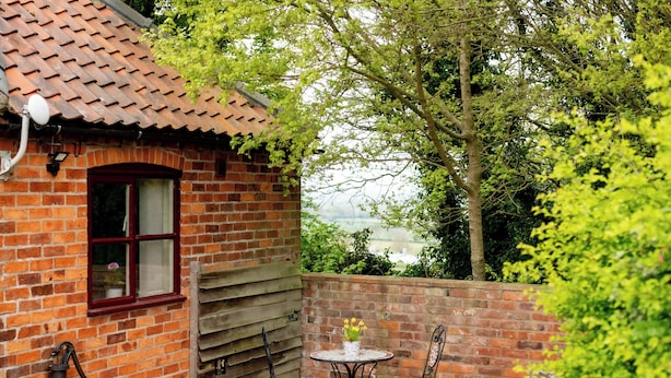 A brick building with a tiled roof, a window, and a small patio area with a table and chairs. - Hill Top Cottage (Lincoln)