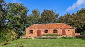 A brick building with a tiled roof, surrounded by a well-maintained lawn and dense trees. - Hill Top Cottage (Lincoln)