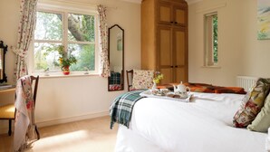 A bedroom with a bed, a wooden wardrobe, a window with curtains, a radiator, and a mirror. - Hill Top Cottage (Lincoln)