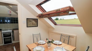 A dining area with a table set for four, a skylight, and a view of a green field. - Uplands (Sherborne)