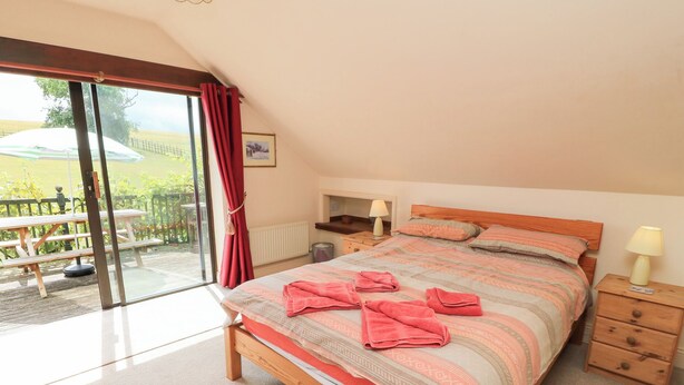 A bedroom with a bed, bedside tables, a window with curtains, and a view of an outdoor area. - Uplands (Sherborne)